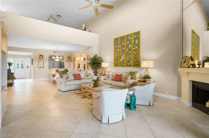 Living room with ceiling fan, light tile patterned floors, a tile fireplace, high vaulted ceiling, and a chandelier
