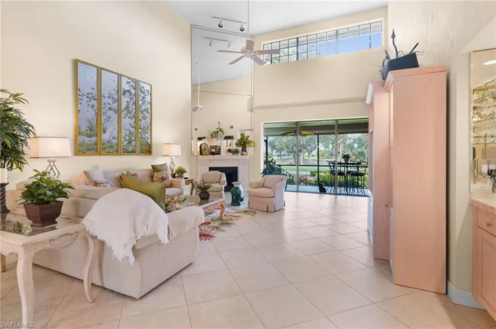 Living room featuring light tile patterned flooring, a high ceiling, a ceiling fan, a fireplace, and a sunroom