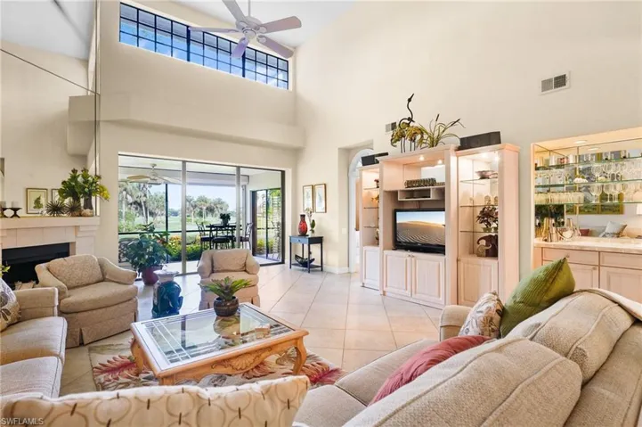 Tiled living room featuring ceiling fan, plenty of natural light, a towering ceiling, and a tiled fireplace
