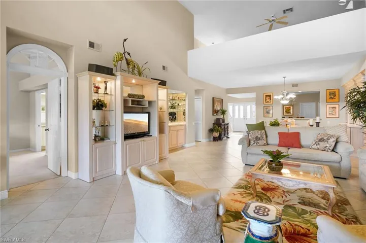 Living room with light tile patterned floors, a ceiling fan, a chandelier, and a high ceiling