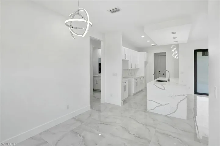 Kitchen featuring white cabinets, hanging light fixtures, light stone countertops, light marble finish floors, and a kitchen island with sink