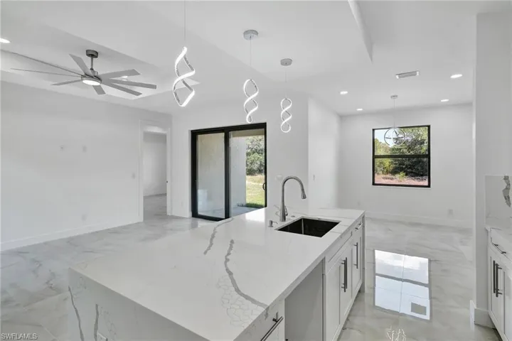 Kitchen with light stone countertops, a kitchen island with sink, and hanging light fixtures