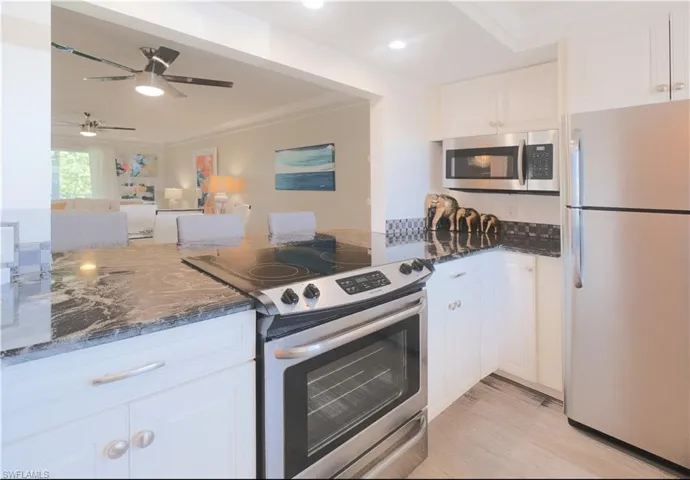 Kitchen with dark stone countertops, ornamental molding, appliances with stainless steel finishes, white cabinets, and ceiling fan