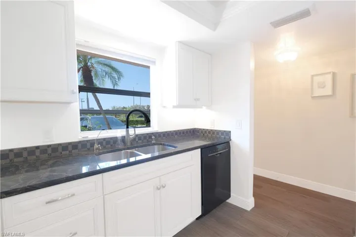 Kitchen featuring tasteful backsplash, dishwasher, dark wood-type flooring, sink, and white cabinetry