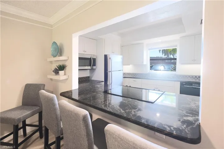 Kitchen with kitchen peninsula, a kitchen bar, black appliances, ornamental molding, and white cabinets