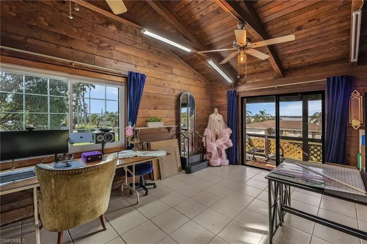 Home office with vaulted ceiling with beams, wood walls, and light tile patterned floors