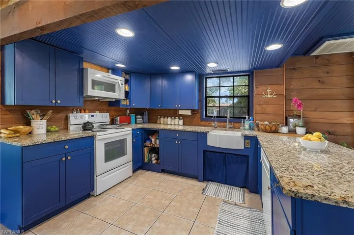 Kitchen with light stone countertops, white appliances, blue cabinets, sink, and light tile patterned floors