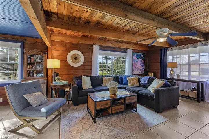 Living room featuring beamed ceiling, light tile patterned floors, wooden walls, and wooden ceiling