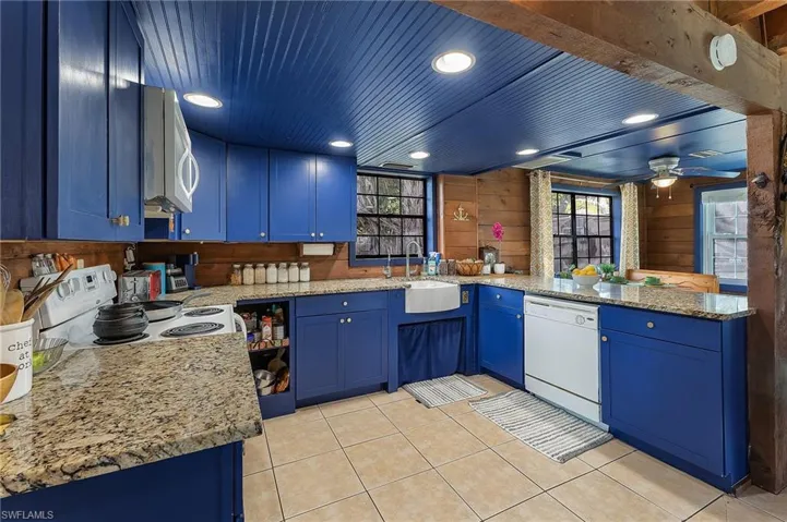 Kitchen with blue cabinetry, sink, kitchen peninsula, wood walls, and white appliances
