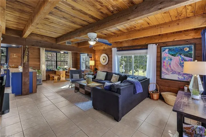 Tiled living room featuring beam ceiling, wooden walls, ceiling fan, and wood ceiling
