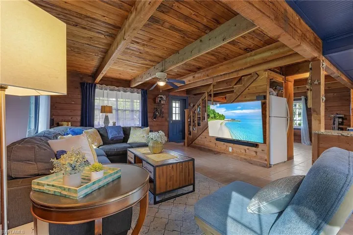 Living room with beamed ceiling, plenty of natural light, ceiling fan, and wooden walls