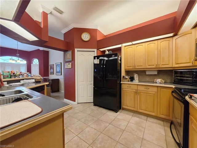 Kitchen featuring black appliances, ornamental molding, backsplash, light tile patterned floors, and decorative light fixtures