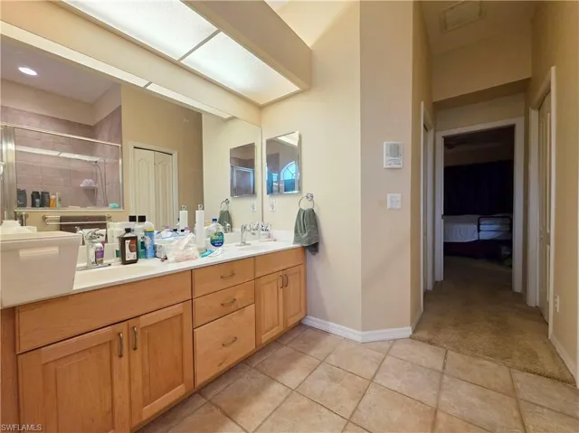 Ensuite bathroom with double vanity, a shower stall, and light tile patterned floors