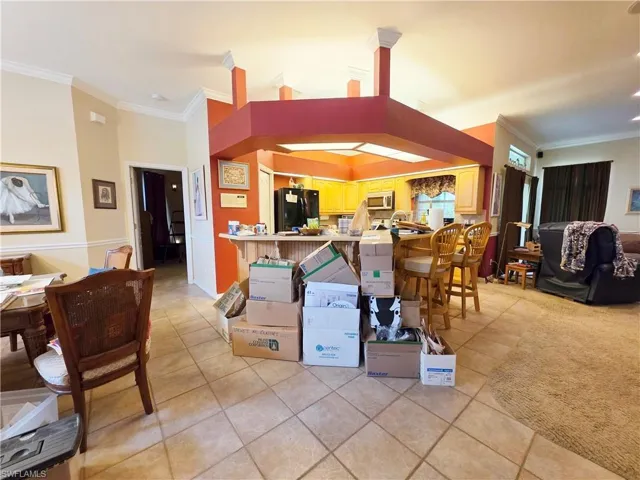 Kitchen with ornamental molding, light tile patterned floors, a breakfast bar area, freestanding refrigerator, and stainless steel microwave
