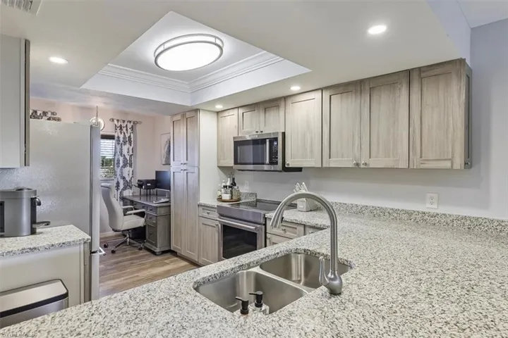 Kitchen with a tray ceiling, stainless steel appliances, light stone countertops, light wood-style floors, and crown molding