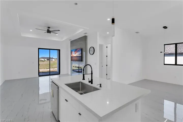 Kitchen featuring open floor plan, white cabinets, decorative light fixtures, a center island with sink, and a raised ceiling
