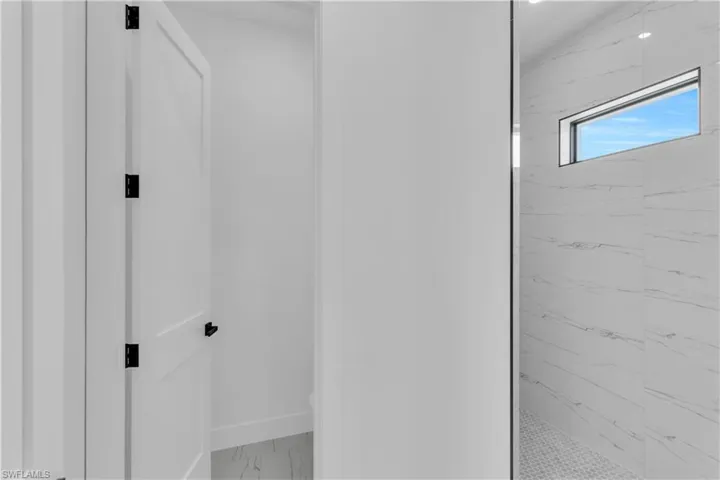 Bathroom with a marble finish shower and light marble finish flooring