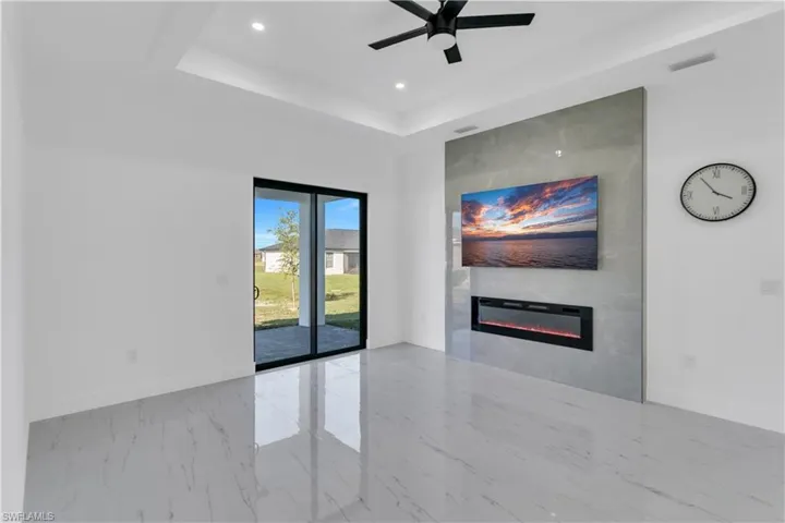 Unfurnished living room featuring a glass covered fireplace, ceiling fan, recessed lighting, marble finish flooring, and a raised ceiling