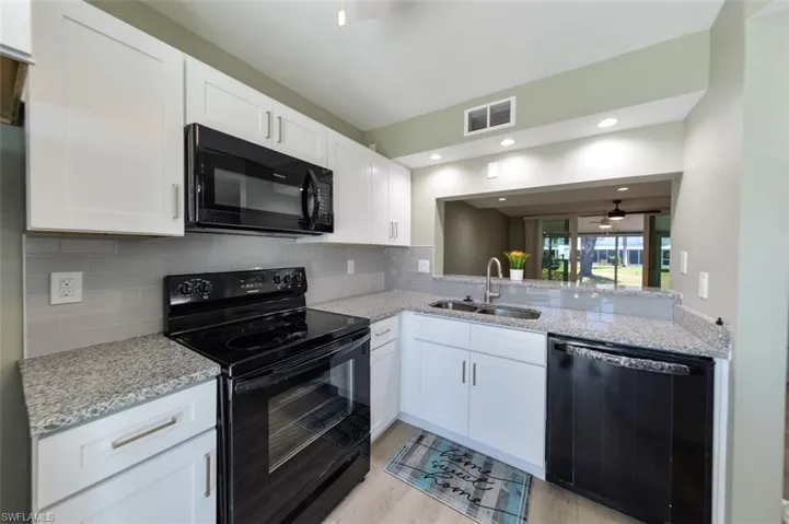Kitchen with tasteful backsplash, light laminate wood-style flooring, black appliances, sink, and white cabinets