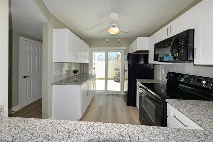 Kitchen with black appliances, white cabinetry, and ceiling fan