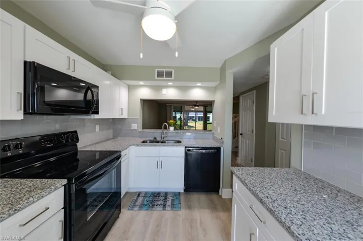 Kitchen featuring backsplash, ceiling fan, black appliances, light laminate wood-style flooring, and sink
