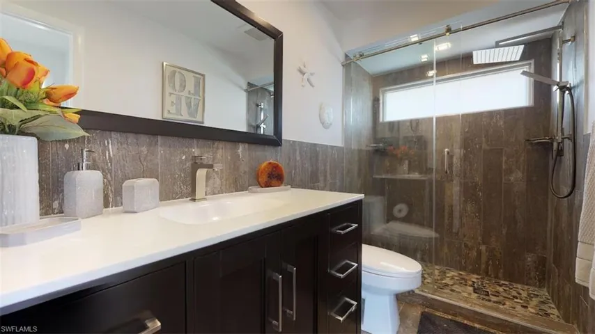 Bathroom featuring vanity, toilet, tile walls, and a tile shower!
