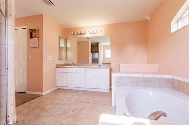 Full bathroom featuring double vanity, a garden tub, plenty of natural light, and light tile patterned floors