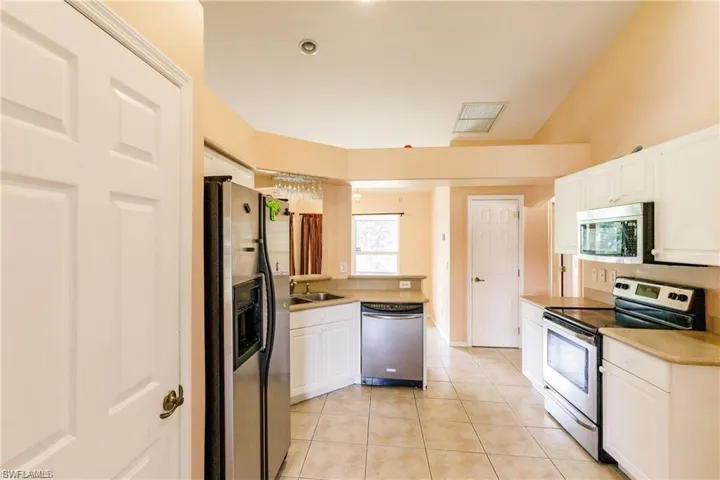 Kitchen featuring stainless steel appliances, light countertops, white cabinets, light tile patterned floors, and a peninsula