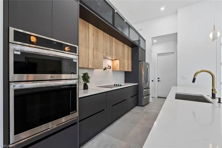 Kitchen with appliances with stainless steel finishes, a sink, modern cabinets, hanging light fixtures, and recessed lighting