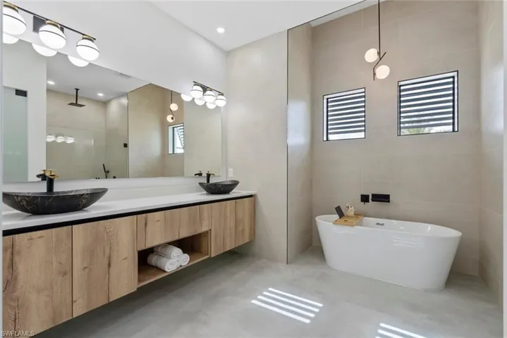 Full bath with tile walls, a freestanding tub, tiled shower, double vanity, and tile patterned flooring