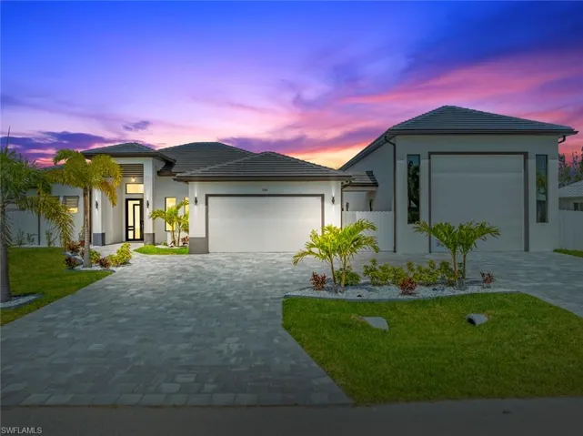 View of front of property featuring a garage, decorative driveway, stucco siding, and a lawn