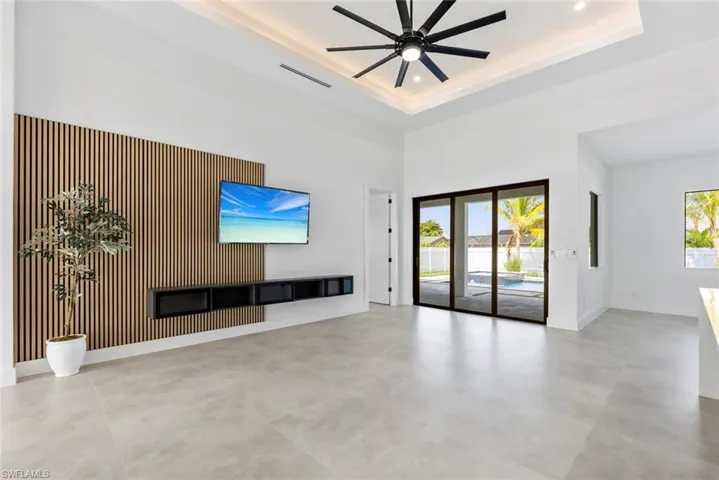 Unfurnished living room featuring baseboards, ceiling fan, a towering ceiling, a raised ceiling, and recessed lighting