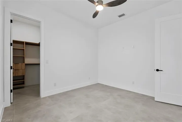 Unfurnished bedroom featuring a walk in closet, baseboards, ceiling fan, and a closet