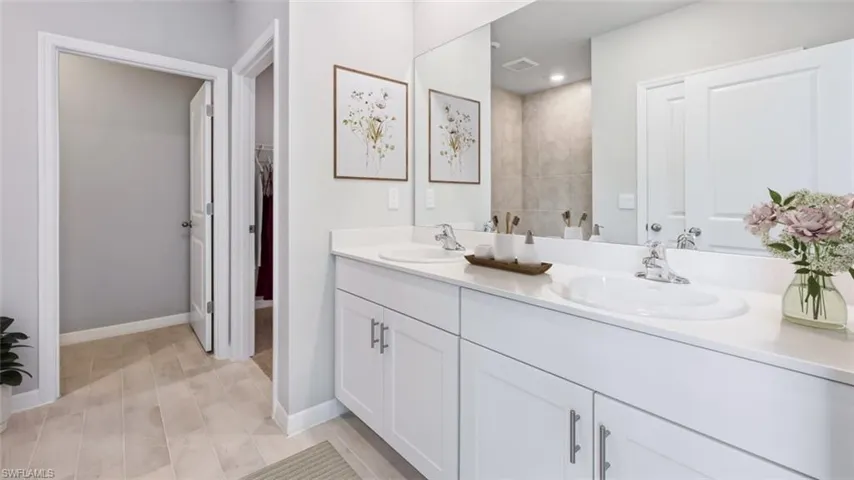 This image is virtually staged. Bathroom featuring double vanity, a walk in closet, and light wood finished floors