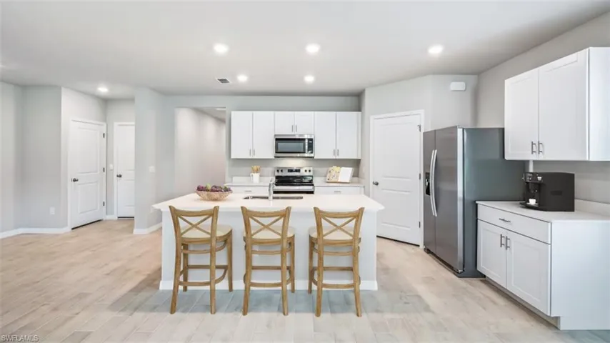 This image is virtually staged. Kitchen featuring a kitchen breakfast bar, white cabinetry, stainless steel appliances, recessed lighting, and a center island with sink