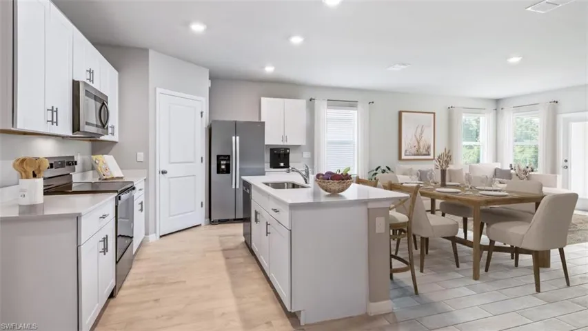 This image is virtually staged. Kitchen featuring stainless steel appliances, white cabinetry, a kitchen island with sink, recessed lighting, and a breakfast bar