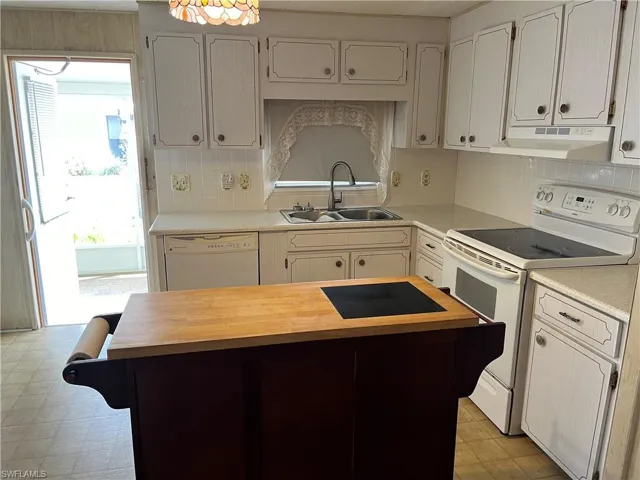 Kitchen featuring light tile patterned flooring, custom range hood, white appliances, backsplash, and sink