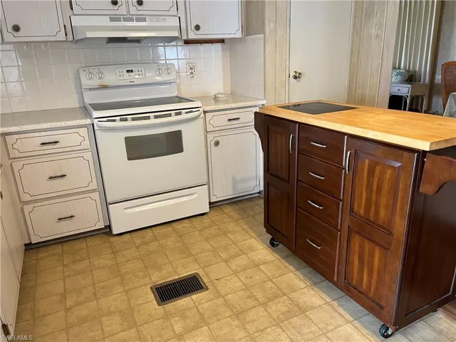 Kitchen featuring light tile patterned flooring, electric range, butcher block counters, and tasteful backsplash
