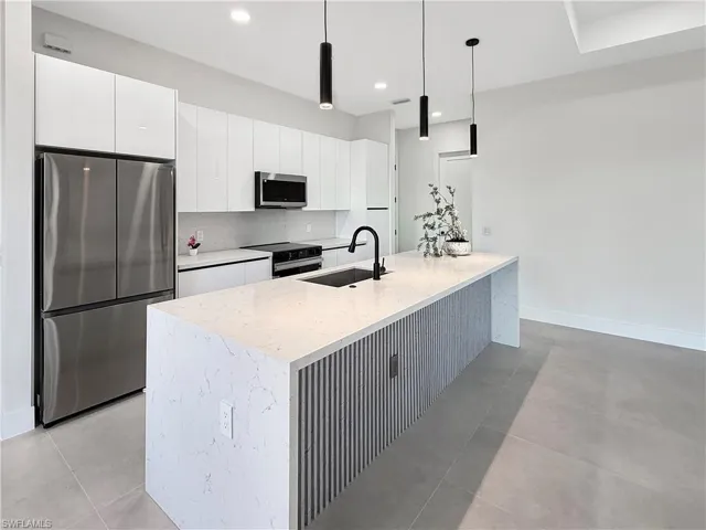 Contemporary kitchen featuring a waterfall island with stone countertop, integrated sink, and matte black faucet