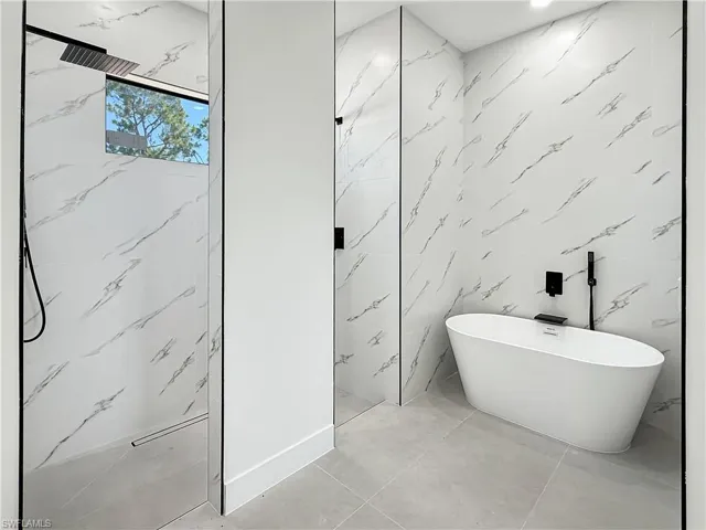 Modern bathroom featuring a freestanding soaking tub with matte black fixtures, a spacious walk-in shower with a rain showerhead, and large format white tile walls with a veined pattern