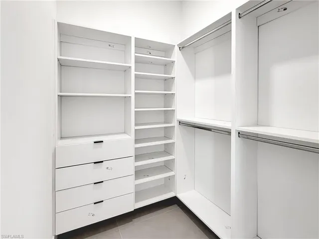 Custom closet system featuring white built-in cabinetry, multiple shelving units, four drawers with contemporary hardware, and integrated hanging rods