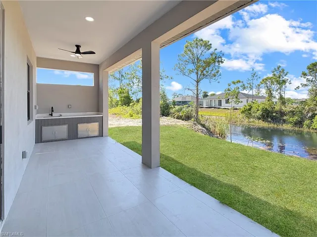Covered outdoor patio featuring light-toned tile flooring, a built-in outdoor kitchen with stainless steel cabinetry and a sink, and a ceiling fan