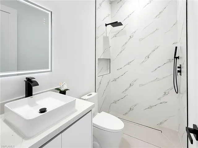 Modern bathroom featuring a rectangular vessel sink with a black faucet, illuminated mirror, and marble-look shower tiling