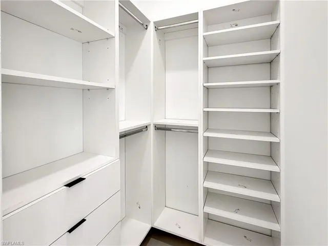 Custom closet system featuring white cabinetry, multiple hanging rods, integrated shelving, and drawers with matte black hardware