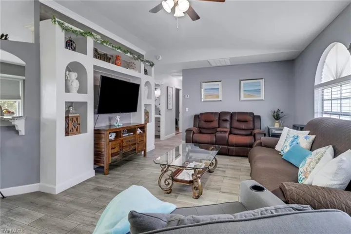 Living room with baseboards, visible vents, ceiling fan, arched walkways, and light wood finished floors