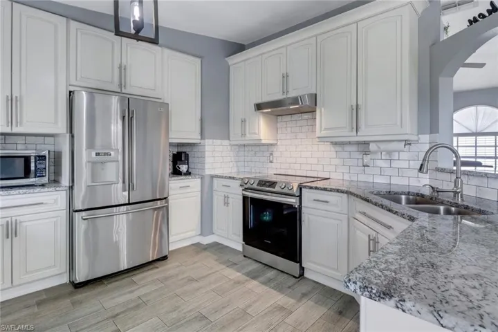 Kitchen featuring light stone countertops, arched walkways, appliances with stainless steel finishes, under cabinet range hood, and a sink