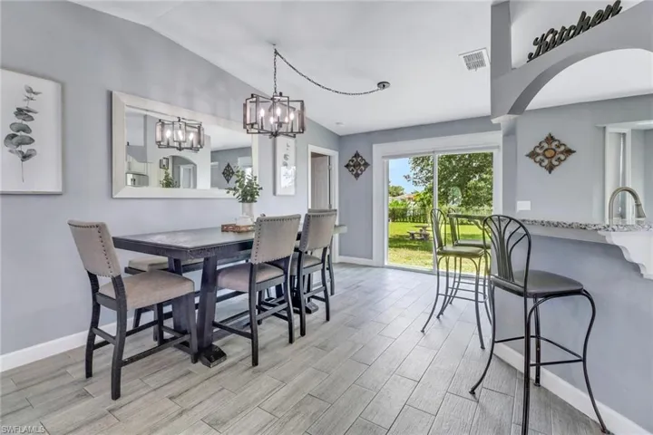 Dining space with light wood-style floors, arched walkways, visible vents, lofted ceiling, and baseboards