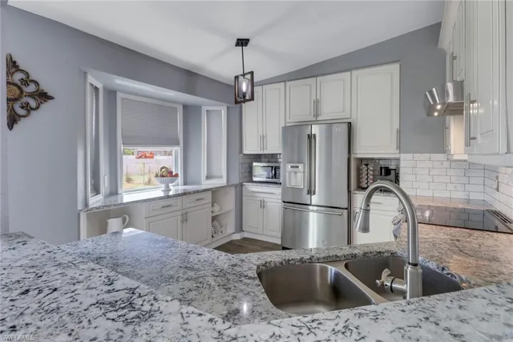 Kitchen featuring appliances with stainless steel finishes, decorative backsplash, a sink, and white cabinets