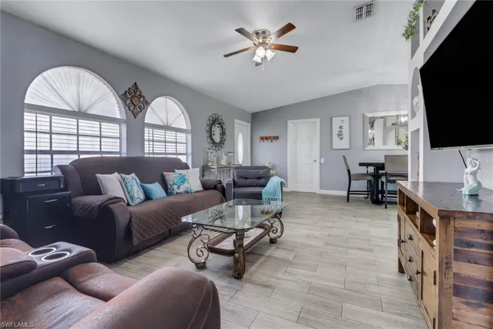 Living room featuring lofted ceiling, visible vents, baseboards, and ceiling fan