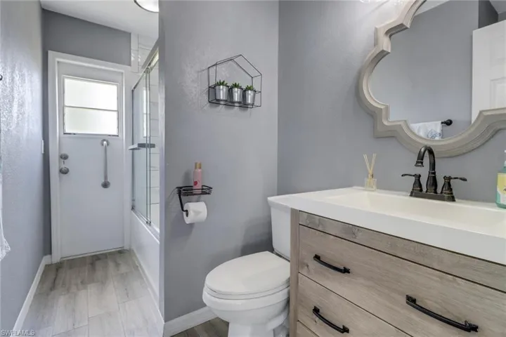 Bathroom with toilet, enclosed tub / shower combo, vanity, and baseboards